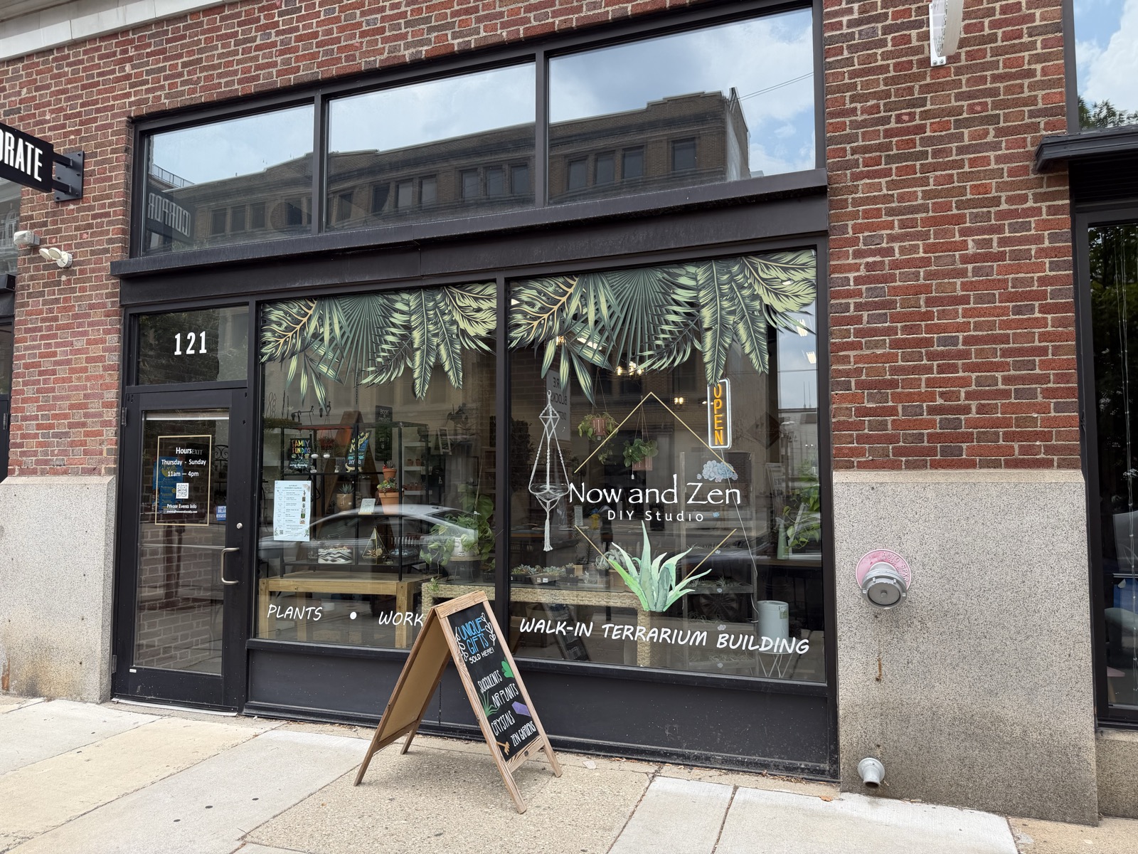 The Now and Zen DIY Studio storefront at 121 in the Fire Blocks District of downtown Dayton, plant-graphic windows and the OPEN sign lit