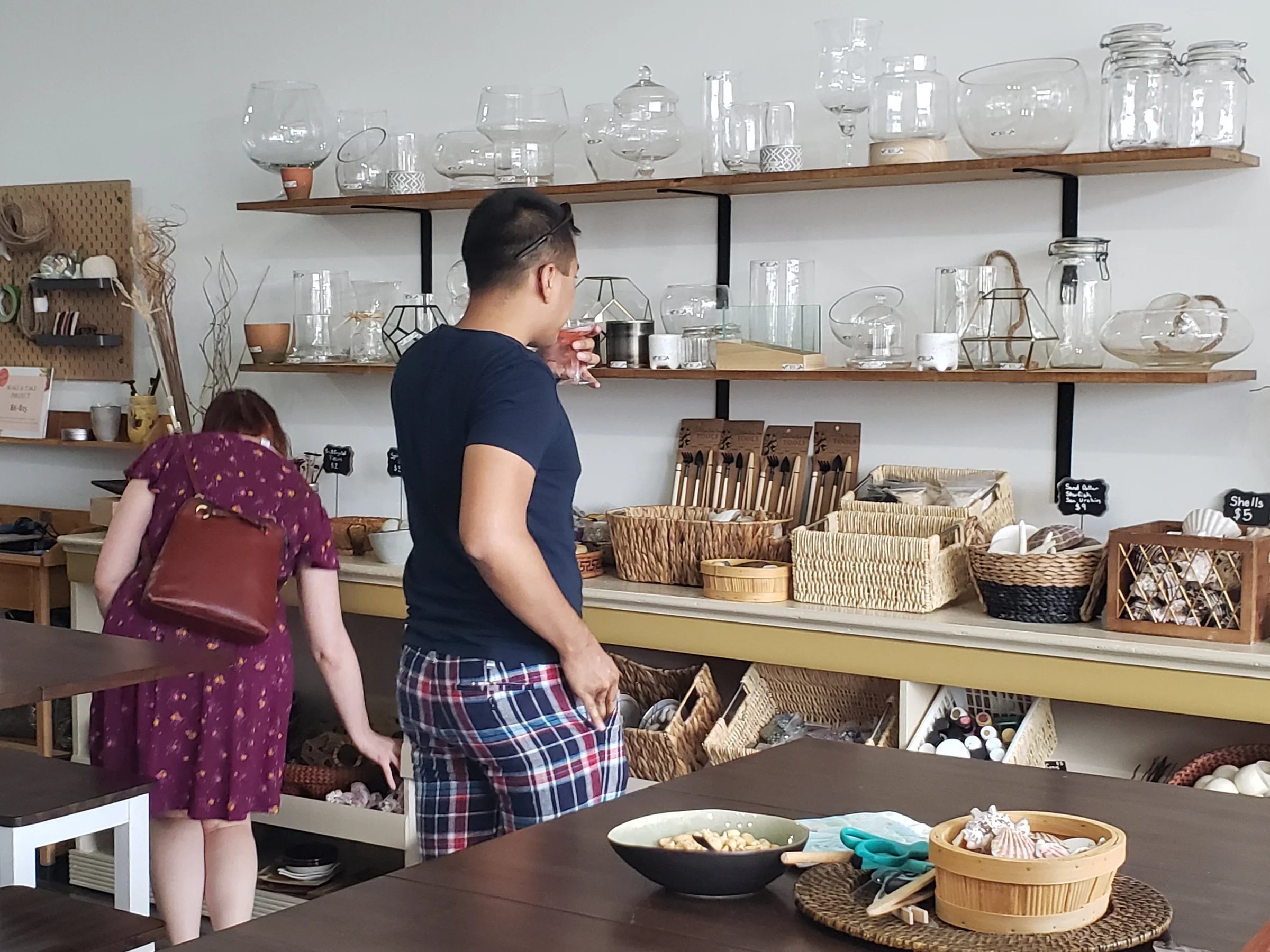 The Terrarium Bar shelves stocked with glass vessels, jars, and tools, with customers browsing and choosing their materials